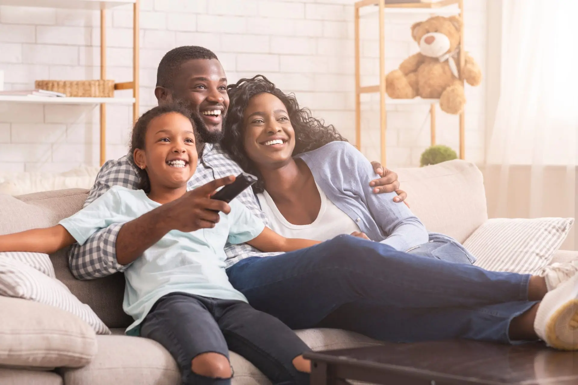 A family of three sitting on a couch and watching TV.